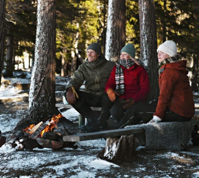 Three people having winter picnic by fire